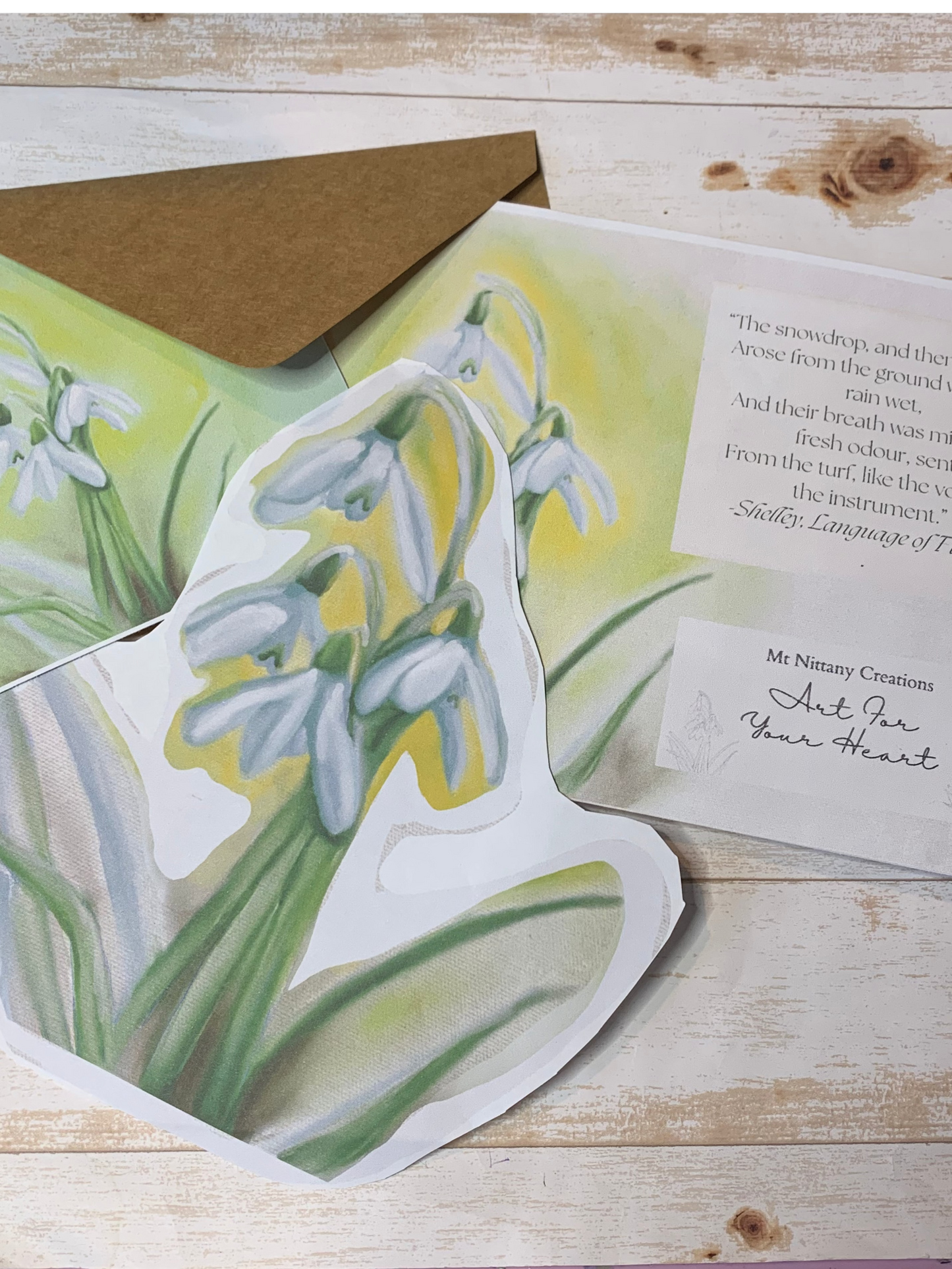 Card with snowdrop illustration and envelope on a wooden surface